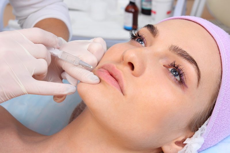 A gloved practitioner injecting a client's lips with a fine syringe