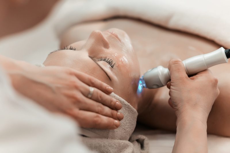 A laser handpiece passing over a client's cheek during a resurfacing treatment